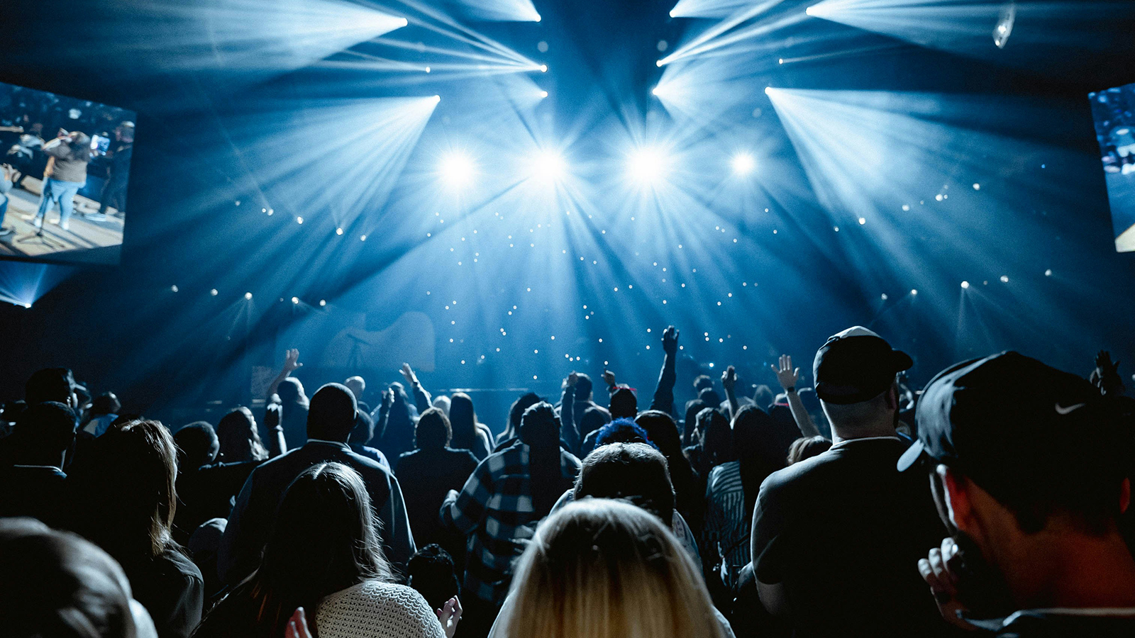 Audience watching a live concert with bright stage lights and raised hands.