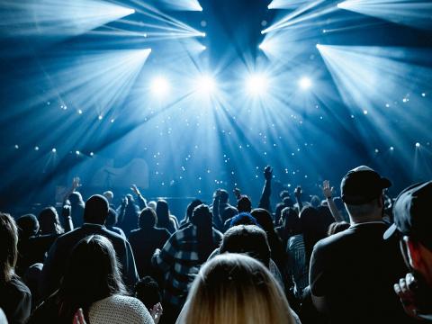 Audience watching a live concert with bright stage lights and raised hands.